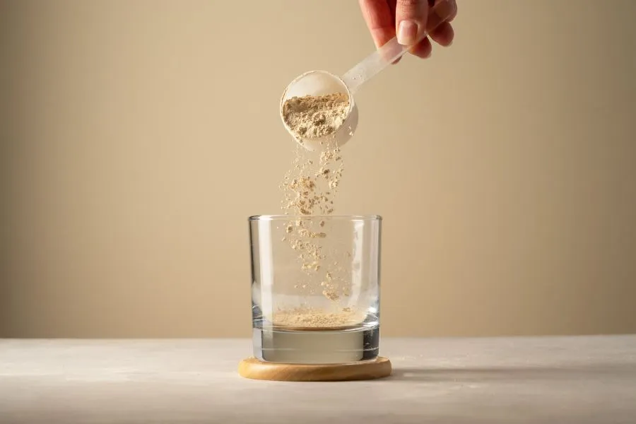 person pouring protein powder into glass